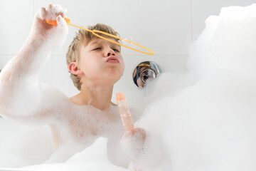 Handsome boy blowing bubbles while taking bubble bath at home. 