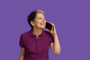 Senior woman with happiness engages in lively conversation on phone. Isolated on violet background,...