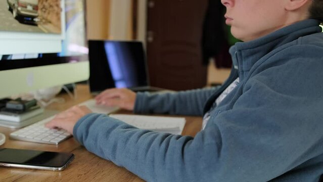 Girl in a cozy home environment works at a personal computer edits video, slow motion shot. Young woman freelancer using keyboard computer at home.