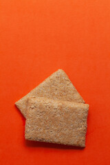Two pieces of Indian mithai (dessert), delicate, soft, crunchy Gajak Bars made of Til, Desi Ghee, and Jaggery.  Top view. On orange background.