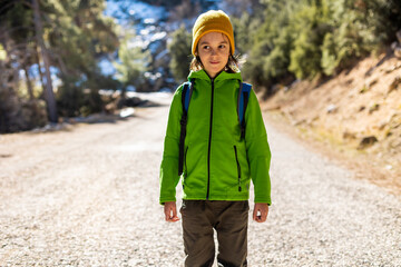 boy with a backpack in the forest. The child is standing in the middle of the road in the forest.
