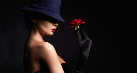 Fototapeta premium Beautiful young Woman In Hat and Gloves holding Flower. Lovely girl with make-up and Red Rose