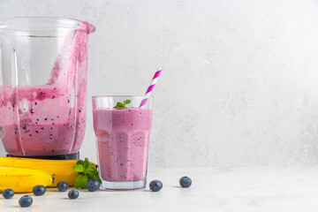 Glass of blueberry and banana smoothie with fresh juicy fruits and blender for making healthy...