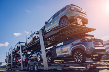 Car carrier trailer transports cars on highway at blue sky background.
