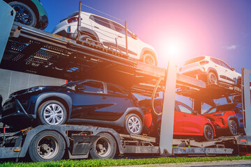 Car carrier trailer transports cars on highway at blue sky background.