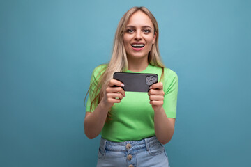 surprised blond girl in casual outfit makes photo using smartphone holding gadget horizontally on...