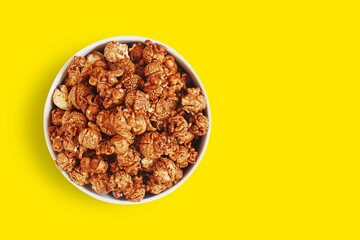 Chocolate caramel sweet popcorn in white bowl isolated on yellow background with clipping path. Top view.