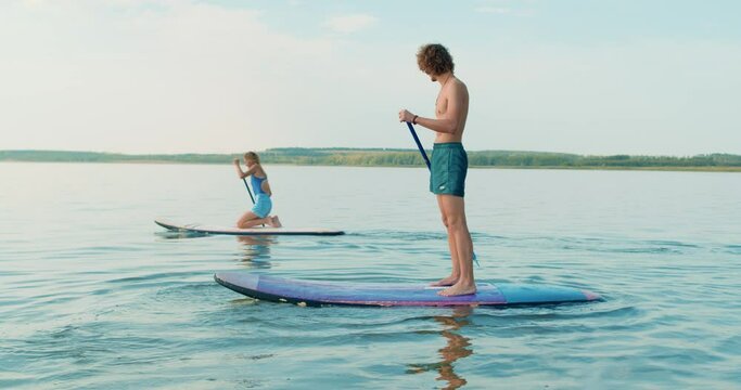 Female and male friends rowing paddleboard in lake. active ambitious couple preparing for SUP surfing competition, Slow motion