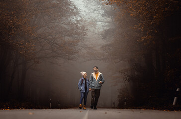 Portrait of couple spending time together walking on forest road on a foggy morning.