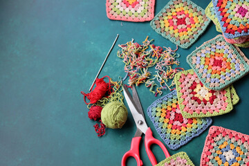 Multicolored Afghan squares, cotton yarn and crochet hook on vibrant blue background with copy...