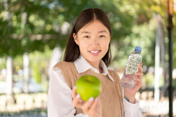 Pretty Chinese woman at outdoors with an apple and with a bottle of water