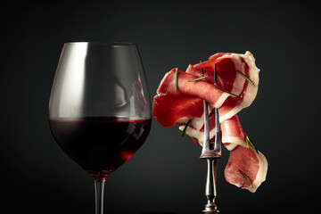 Glass of red wine and sliced prosciutto with rosemary.
