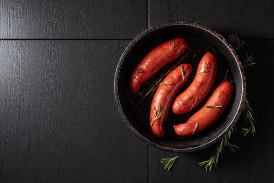 Roasted Bavarian sausages with rosemary in an old black pan.