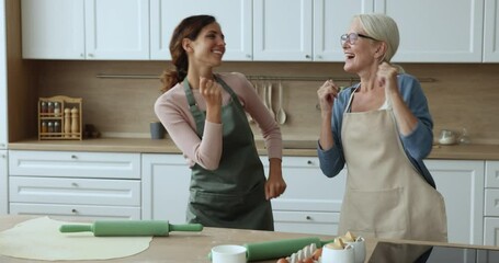 Two women older and younger, elderly mom her young grown up daughter fooling around dancing to favourite music, singing popular song relish family weekend at home, having good relations enjoy pastime
