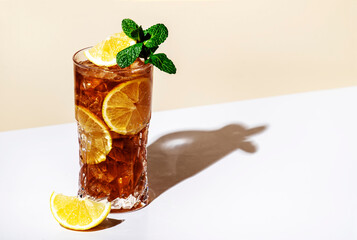 Long Island ice tea cocktail drink with vodka, rum, tequila, gin, liquor, lemon juice, cola and ice with lemon slice and mint in highball glass. Beige background, hard light, minimalism