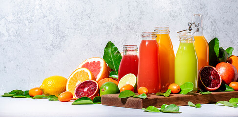 Summer fruit juices and smoothies, food background. Mix of different whole and cut fruits: orange, grapefruit, lime, tangerine with leaves and bottles with drinks. Copy space banner