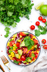 Spicy salad with sweet corn, red beans, avocado, jalapeno, cherry tomatoes, red onion and cilantro. White table background, top view