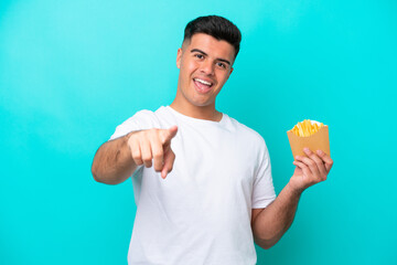 Young caucasian man catching french fries isolated on blue background surprised and pointing front