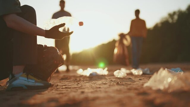 Guys volunteers cleaning sandy beach collecting trash garbage near ocean at sunset. Ecology lifestyle, environment pollution and protection. Putting on trash, rubbish, waste, junk in plastic bags.