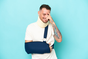 Young caucasian man wearing a sling  and neck lace isolated on blue background laughing