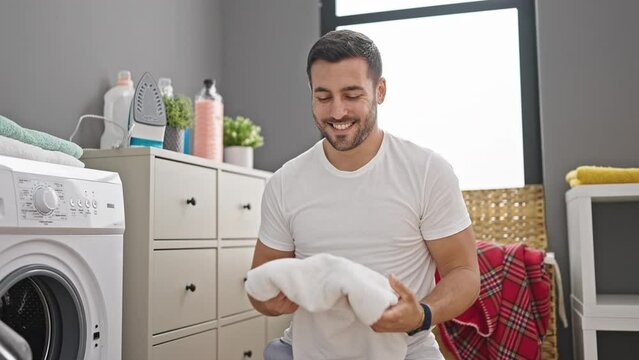 Young hispanic man smiling confident smelling clothes at laundry room