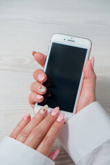 Women's hands with pink manicure are holding a white smartphone with an empty screen.