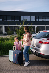 Mom and daughter stand near the car with their suitcases and waiting for the trip. Family journey 