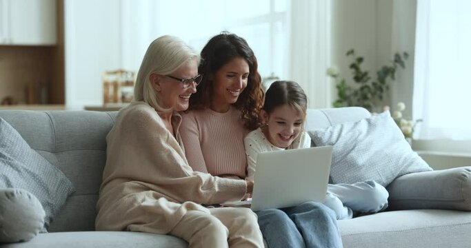 Friendly loving multigenerational family of women spend free time at home with laptop, watch funny video, use educational appl for kids, shopping through retail e-services, enjoy warm relationships