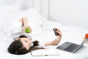Young woman in the white shirt and pajama relaxing lying on a bed, she using mobile phone play social.