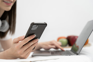 Young woman in the white shirt and pajama relaxing lying on a bed, she using mobile phone play social.
