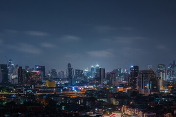 Fototapeta premium City scape night time of Bangkok, Thailand. on blue sky and cloud backgroundTall building in the night and line of light car in the extra road urban.Long exprossure.