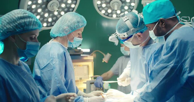 Multiracial team of professional medical surgeons performs surgical operation in modern hospital. Male and female doctors are working to save patient. Concept of medicine and treatment.