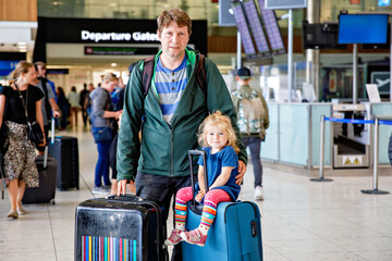 Cute little toddler girl and father at the airport. Happy family traveling by plane, making...