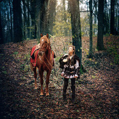 Nordic Viking Warrior Woman and Her Majestic Horse Embrace the Forest in Medieval Scene Reconstruction, Showcasing Traditional Attire with Fur Collar, War Makeup, and a Glimpse