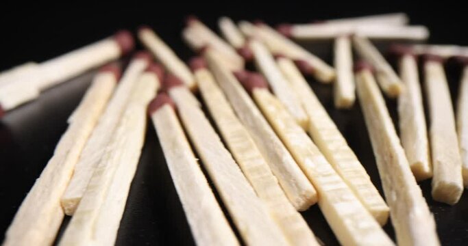 Thin aspen matches with red sulfur heads scattered randomly on black table in dark premise. Wooden matchsticks for getting fire or cooking purposes