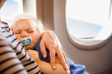 Woman traveling with little child by airplane. Sad tired toddler girl sitting with mum by aircraft...