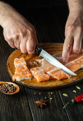 The cook cuts fresh red fish with a knife on a wooden cutting board. Homemade delicious fish dish according to an old recipe