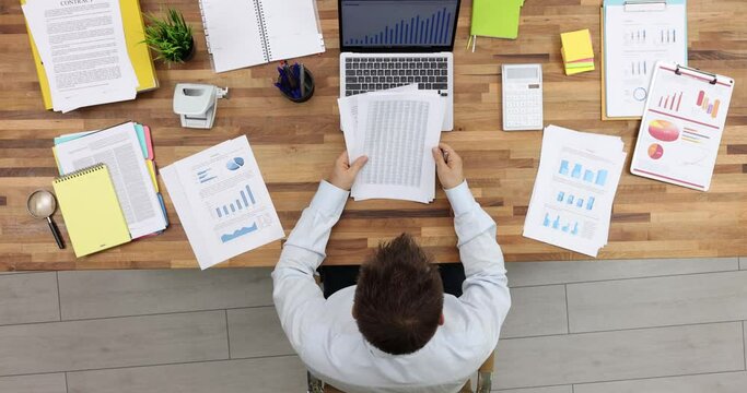 Male employee examines documents with diagrams circling relevant information. Man creates strategy of company development slow motion