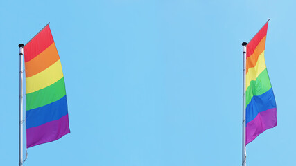 two vertical rainbow or lgbtq pride flags fly on flagpole against blue sky with copy space