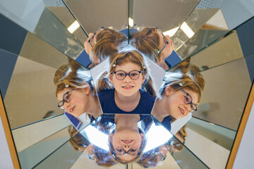 Little child playing with mirrors. Happy preschool girl with glasses having fun with experiments,...