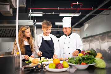 A group of male and female students are learning to cook in the kitchen of a cooking school.