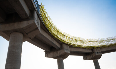 A low-angle photograph of a concrete pedestrian walkway with yellow metal rails, showing robust concrete engineering elements