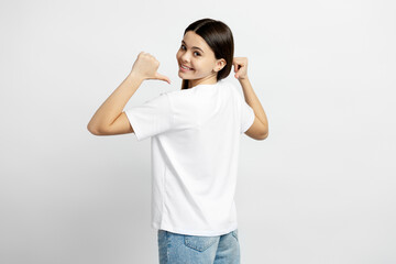 Obraz na płótnie Canvas Portrait of smiling latin teenage girl wearing white t shirt pointing fingers at mockup isolated on white background. Shopping concept