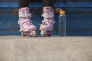 Young skater girl sitting on a ledge in a skatepark with glass water bottle. Feet of unrecognizable...