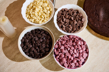 Overhead view of bowls with drops of various belgian confectionery dark, milk, white and ruby pink chocolate chips. Organic food ingredient. Still life. Confectionery. Sweet food