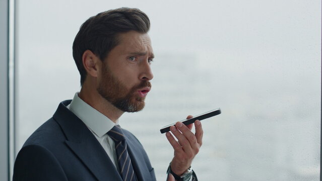 Closeup annoyed businessman recording voice message on speakerphone at office.