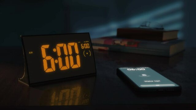 Digital alarm clock with orange clockface and the smartphone waking up at 6 AM. The numbers on the clock screen changes from 5:59 no 6:00 AM. And the alarm goes off on the phone. Close up view.