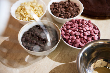 View through blurred whisk of a food processor of various chips of white, dark, ruby, and caramel organic chocolate in bowls on the kitchen countertop