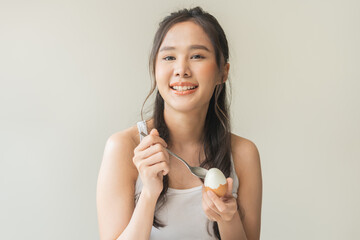 Obraz na płótnie Canvas Protein in food, happy smiling asian young woman, girl in diet holding boiled fresh egg, eat with spoon for breakfast in living room in the morning at home. Health care, loss weight people concept.