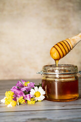 Honey jar with honey dipper next to some flowers